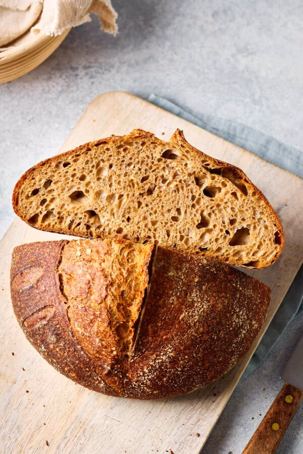 Dinkel-Sauerteigbrot aufgeschnitten auf einem Holzbrett mit sichtbarer lockerer Krume.