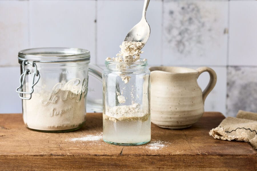 Mehl wird in eine Einmachglas mit Wasser und Sauerteiganstellgut gegeben, um den Sauerteig zu füttern.