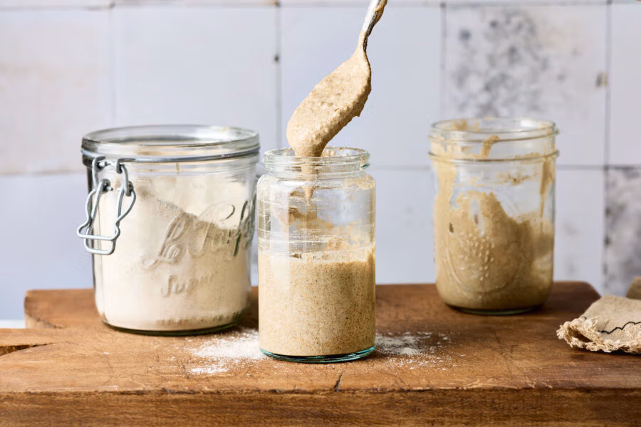 Mehl wird in ein Weckglas mit Wasser und Sauerteig gegeben und eingerührt.