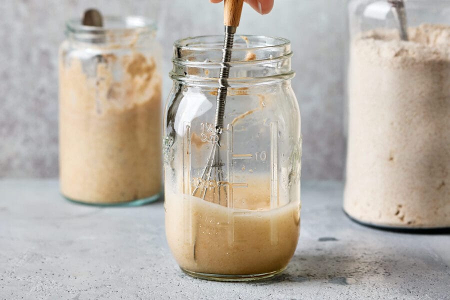 Sauerteig anstellgut wird in einem Glas mit lauwarmen Wasser verrührt.