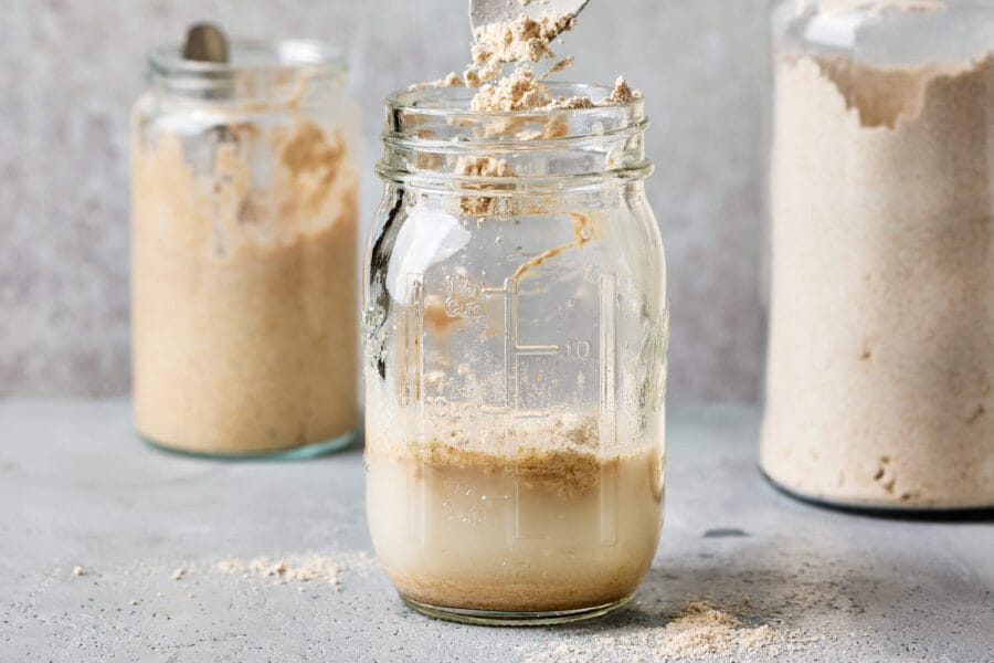 Mehl wird in eine Einmachglas mit Wasser und Sauerteiganstellgut gegeben, um den Sauerteig zu füttern.