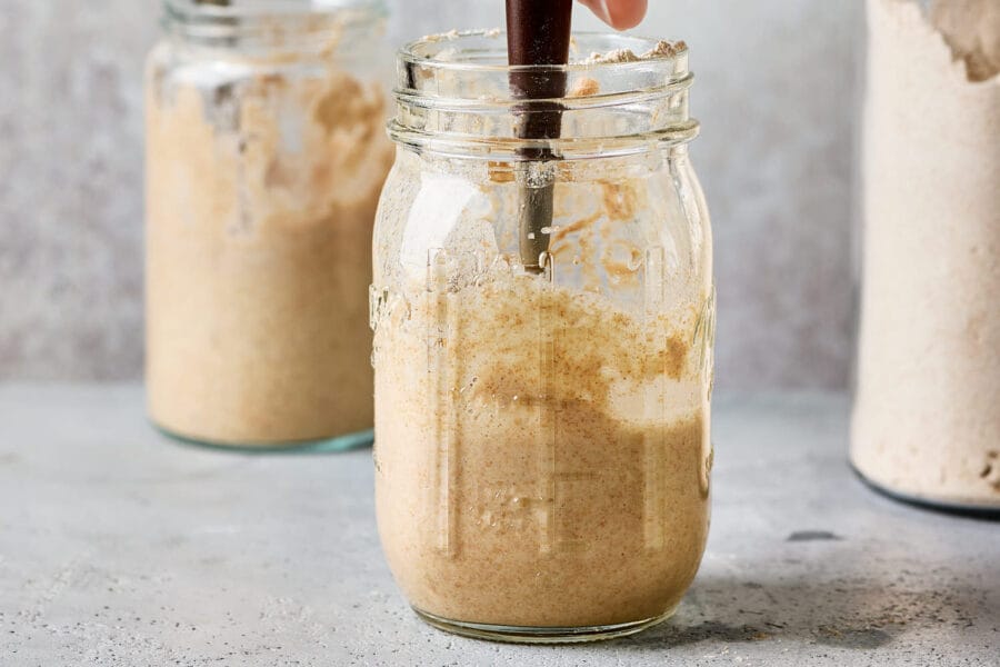 Mehl wird in ein Weckglas mit Wasser und Sauerteig gegeben und eingerührt.