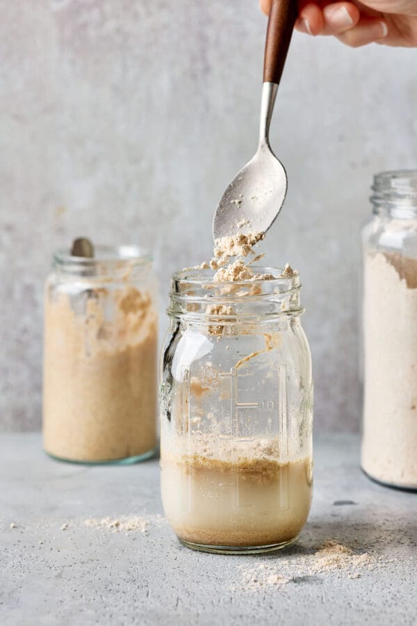 Mehl wird in eine Einmachglas mit Wasser und Sauerteiganstellgut gegeben, um den Sauerteig zu füttern.