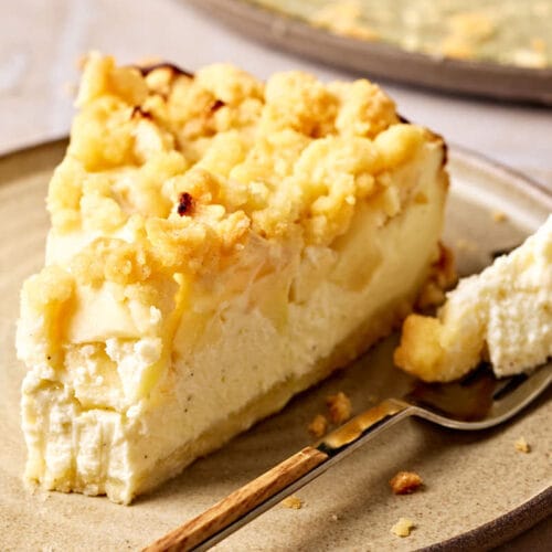 Saftiger Apfelkuchen mit Quark und Streusel auf einem Teller, mit einem Stück Kuchen im Vordergrund.