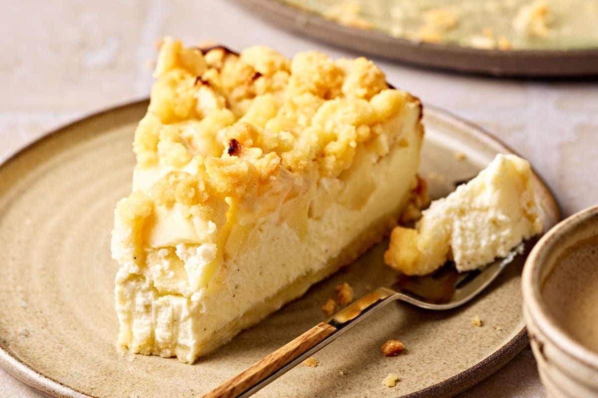 Saftiger Apfelkuchen mit Quark und Streusel auf einem Teller, mit einem Stück Kuchen im Vordergrund.