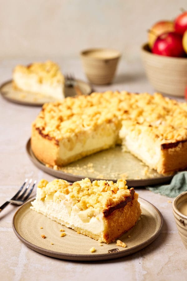 Saftiger Apfelkuchen mit Quark und Streusel auf einem Teller, mit einem Stück Kuchen im Vordergrund.