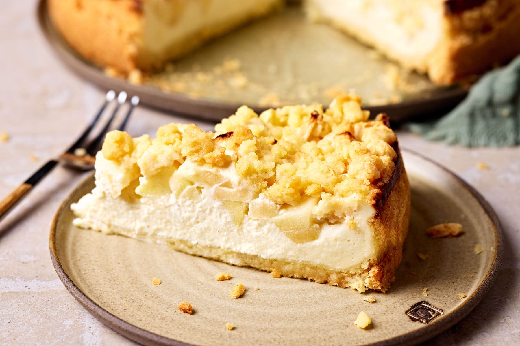 Saftiger Apfelkuchen mit Quark und Streusel auf einem Teller, mit einem Stück Kuchen im Vordergrund.