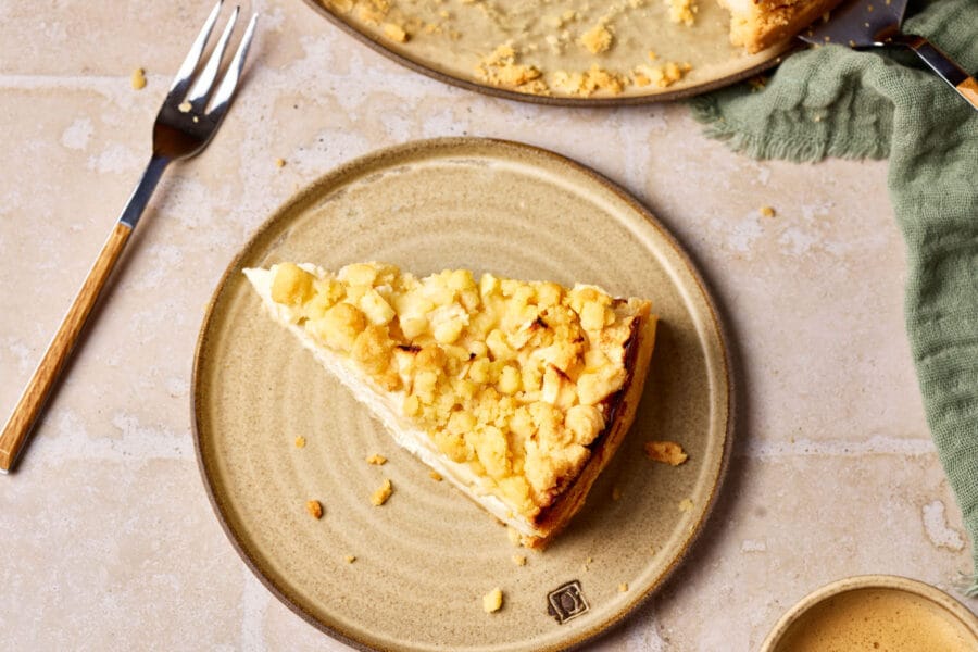 Saftiger Apfelkuchen mit Quark und Streusel auf einem Teller, mit einem Stück Kuchen im Vordergrund.