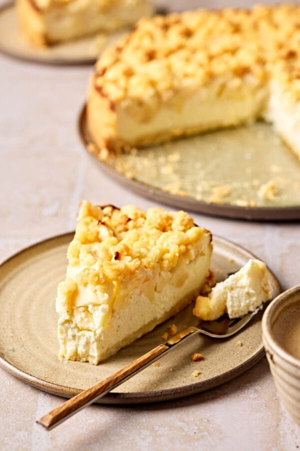 Saftiger Apfelkuchen mit Quark und Streusel auf einem Teller, mit einem Stück Kuchen im Vordergrund.