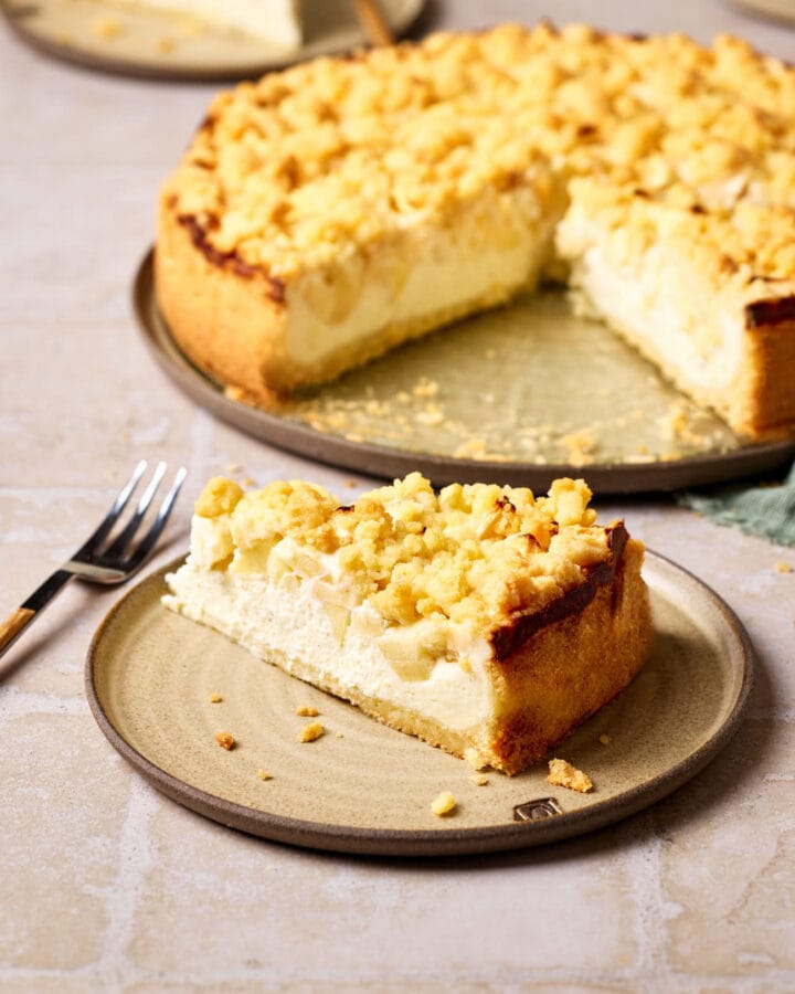 Saftiger Apfelkuchen mit Quark und Streusel auf einem Teller, mit einem Stück Kuchen im Vordergrund.