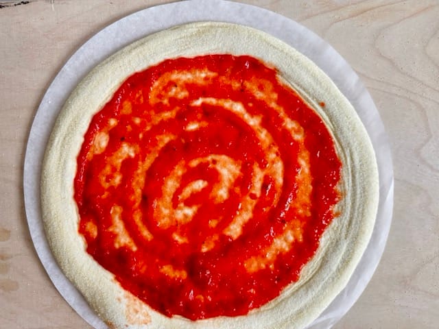 Pizzateig, mit Tomatensoße belegt, vor dem Backen.