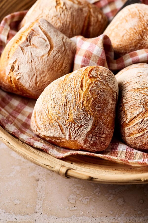 Knusprige Sauerteigbrötchen in einem Brötchenkorb mit einem karierten Tuch darunter.