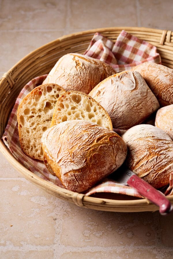 Knusprige Sauerteigbrötchen mit lockerer Krume in einem Brötchenkorb mit einem karierten Tuch darunter.