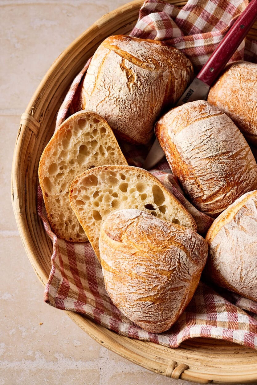 Knusprige Sauerteigbrötchen mit lockerer Krume in einem Brötchenkorb mit einem karierten Tuch darunter.