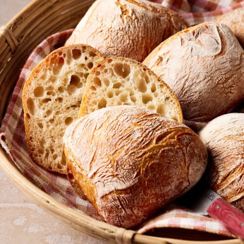 Knusprige Sauerteigbrötchen mit lockerer Krume in einem Brötchenkorb mit einem karierten Tuch darunter.