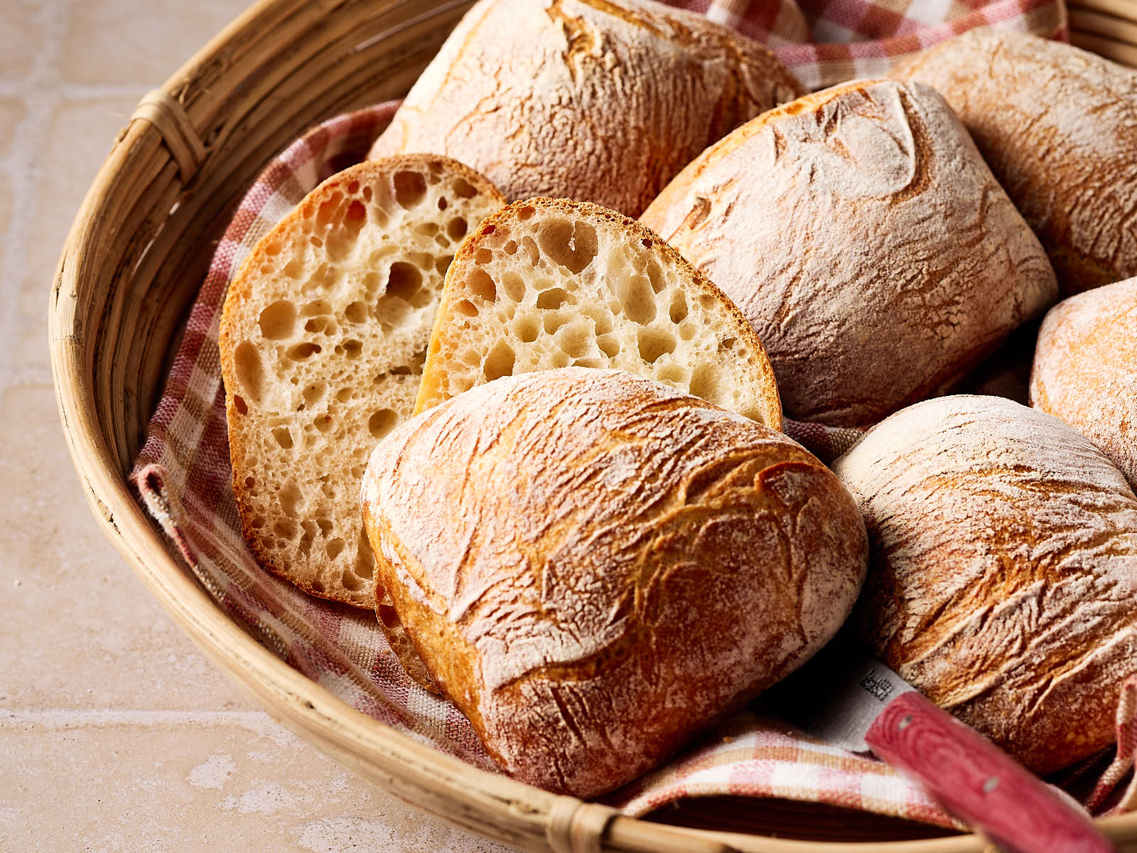 Knusprige Sauerteigbrötchen mit lockerer Krume in einem Brötchenkorb mit einem karierten Tuch darunter.