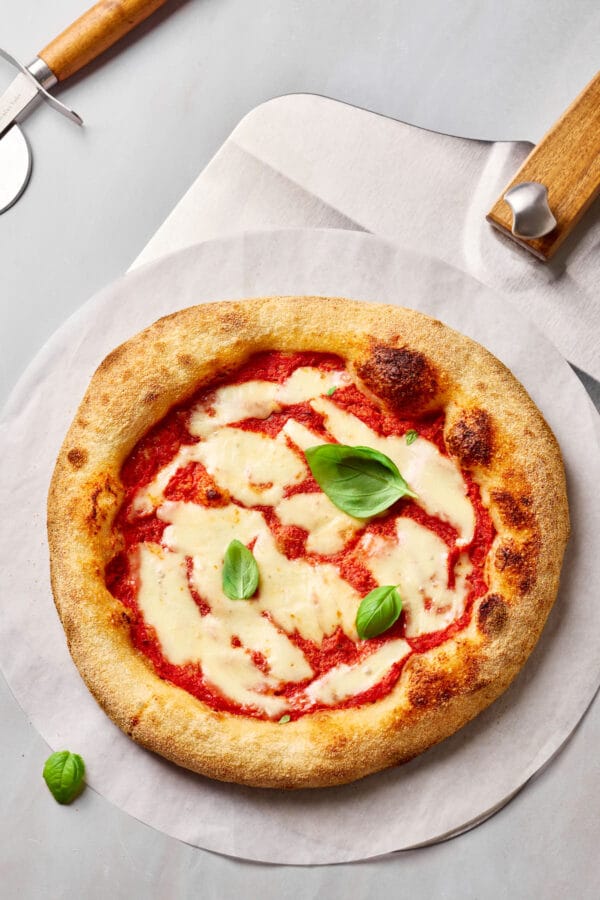 Sauerteig-Pizza mit knusprigem Rand auf Backstahl gebacken, mit luftigem Rand auf einem Brotschieber.