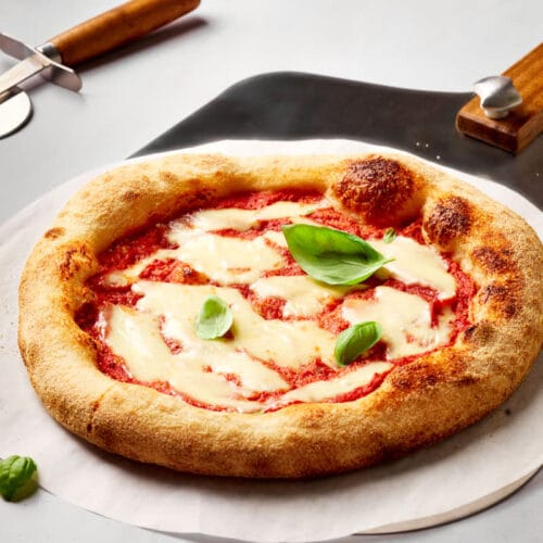 Sauerteig-Pizza mit knusprigem Rand auf Backstahl gebacken, mit luftigem Rand auf einem Brotschieber.