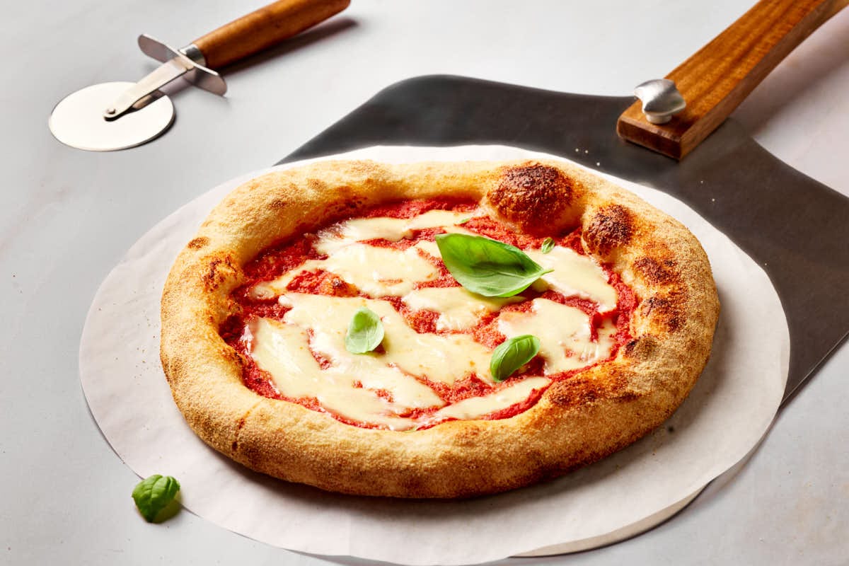 Sauerteig-Pizza mit knusprigem Rand auf Backstahl gebacken, mit luftigem Rand auf einem Brotschieber.