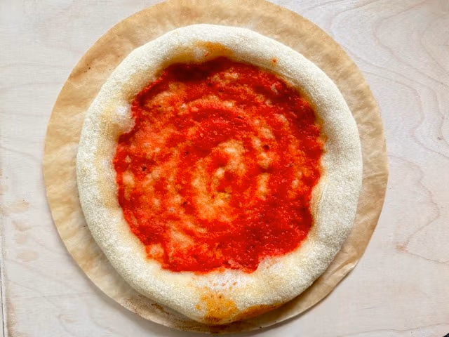 Mit Tomatensoße vorgebackene Pizza vor dem endgültigen Belegen.