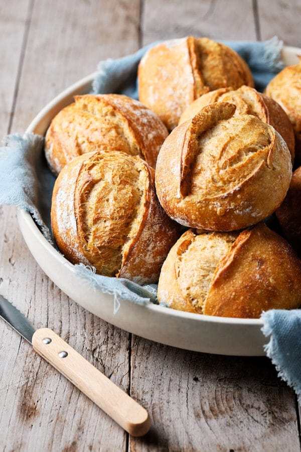 Dinkelbrötchen mit Sauerteig in einer Keramikschale, mit einem Tuch darunter und einem Messer daneben.