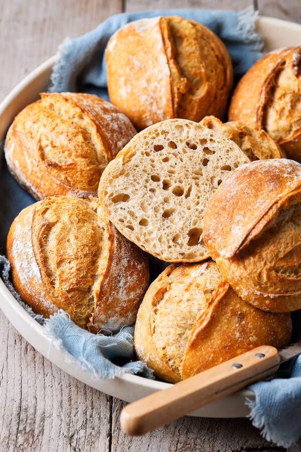 Dinkelbrötchen mit Sauerteig in einer Keramikschale, mit einem Tuch darunter und einem Messer daneben.