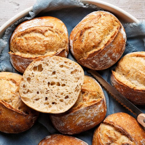 Dinkelbrötchen mit Sauerteig in einer Keramikschale, mit einem Tuch darunter und einem Messer daneben.