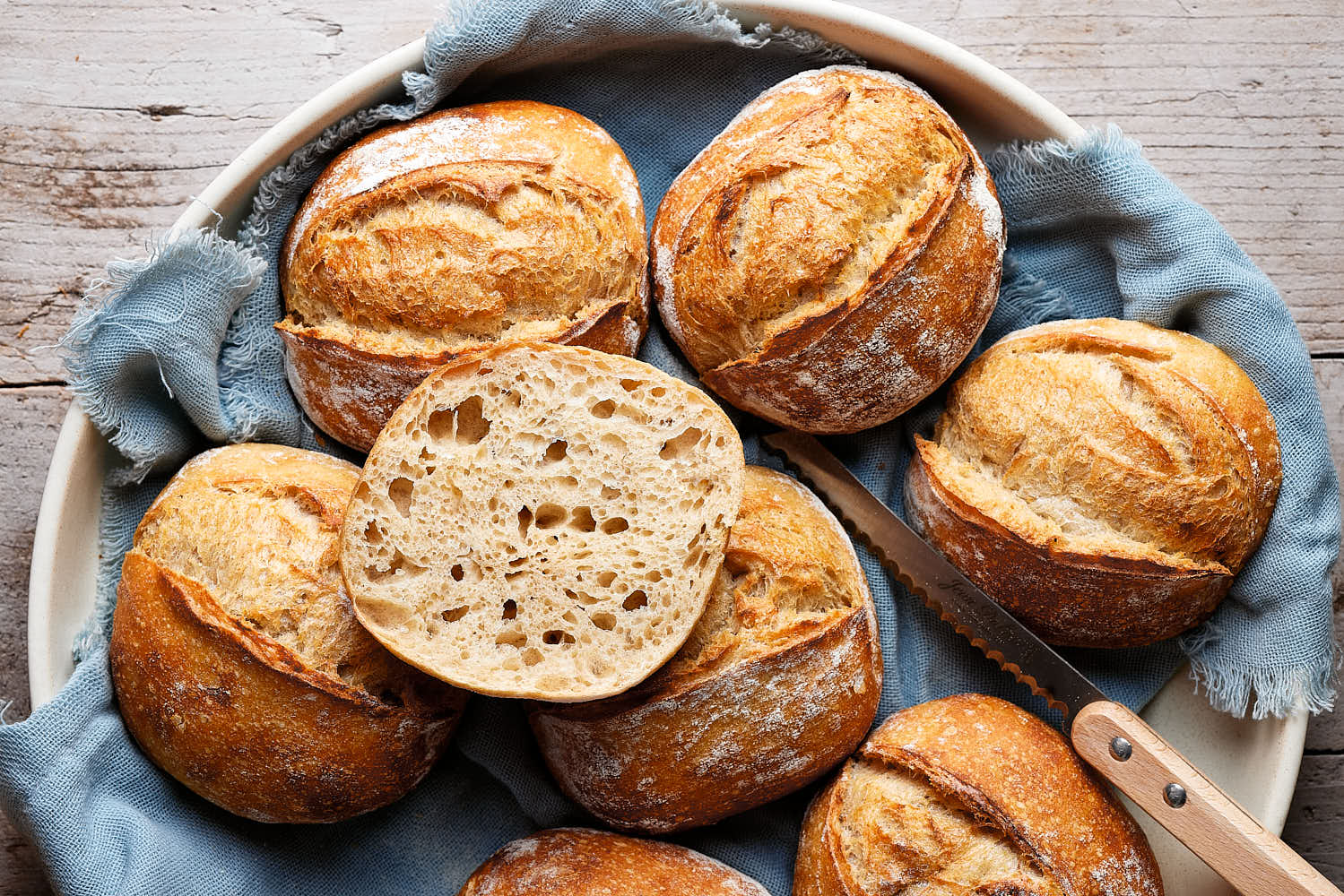 Dinkelbrötchen mit Sauerteig in einer Keramikschale, mit einem Tuch darunter und einem Messer daneben.