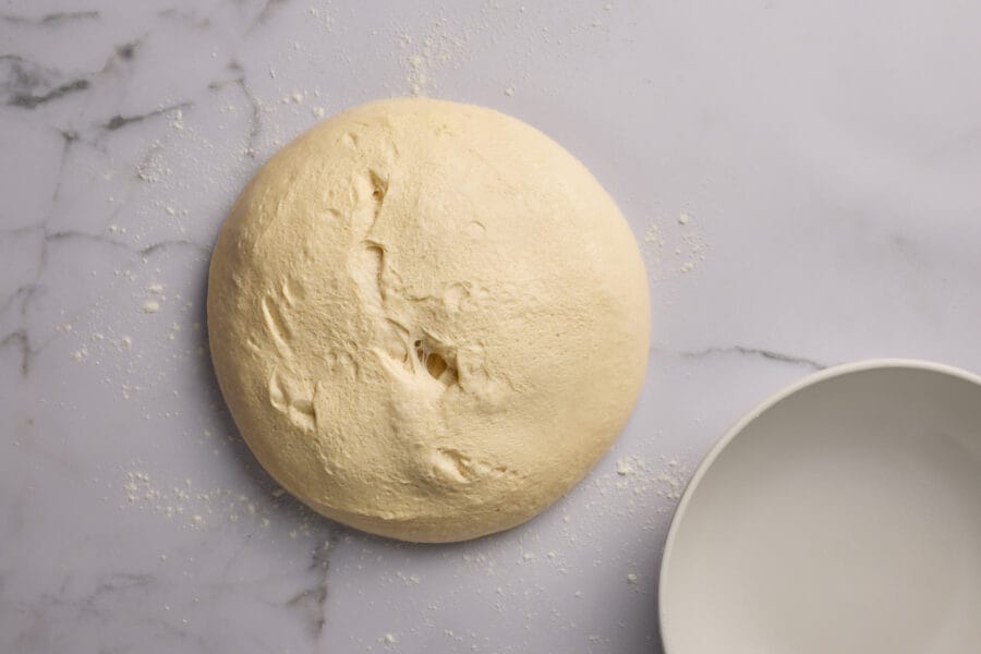 Ausgekippter Hefeteig auf einer Marmorfläche mit einer leeren Teigschüssel daneben.