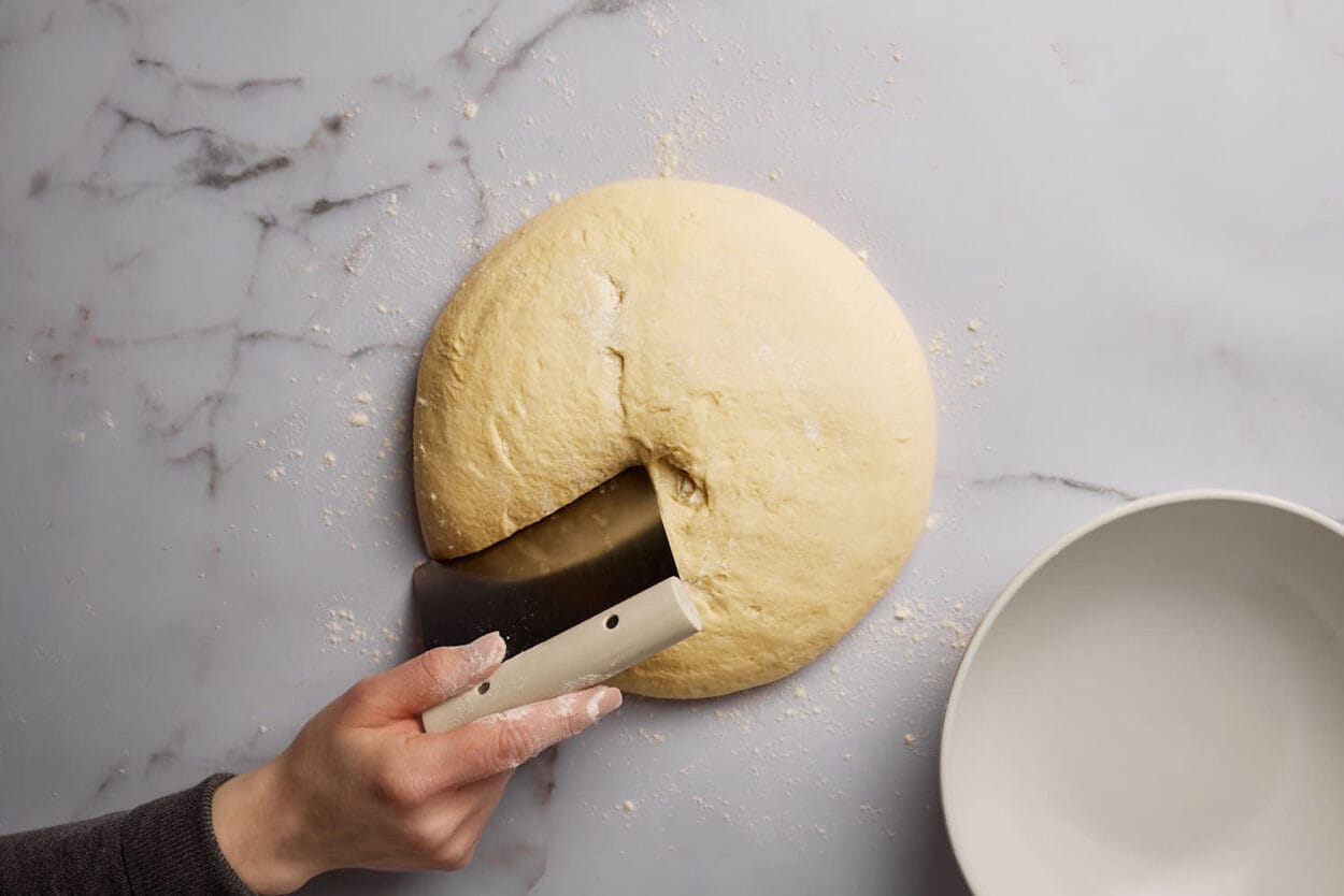 Hefeteig auf einer Marmorplatte, der mit einer Teigkarte geteilt wird.