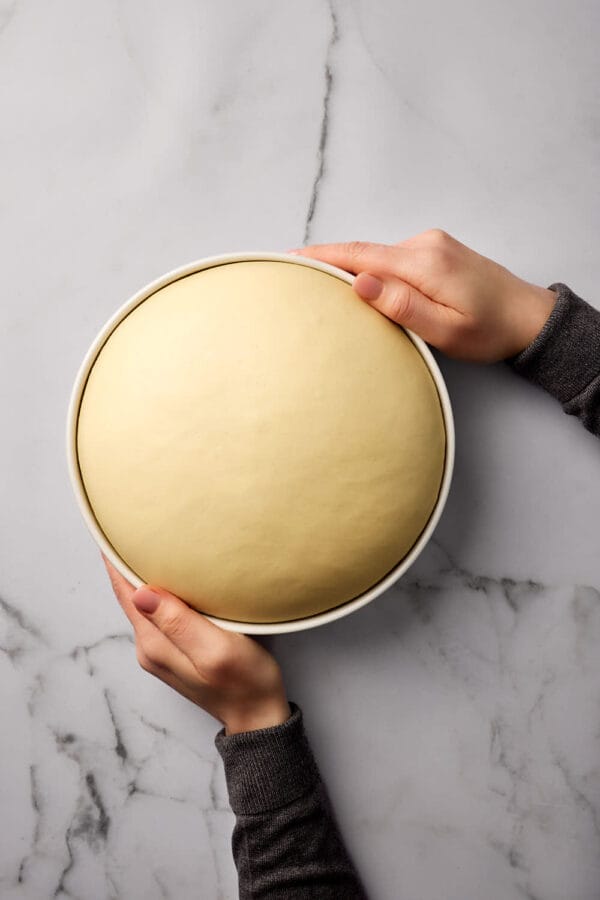 Hefeteig in einer Keramikschüssel, die von zwei Händen gehalten wird.