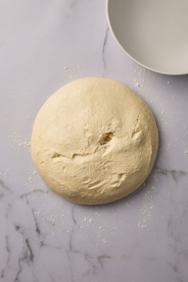 Ausgekippter Hefeteig auf einer Marmorfläche mit einer leeren Teigschüssel daneben.