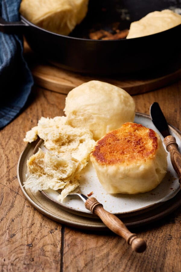 Dampfnudeln mit Salzkruste auf einem Teller mit lockerer Krume und Holzbesteck daneben.