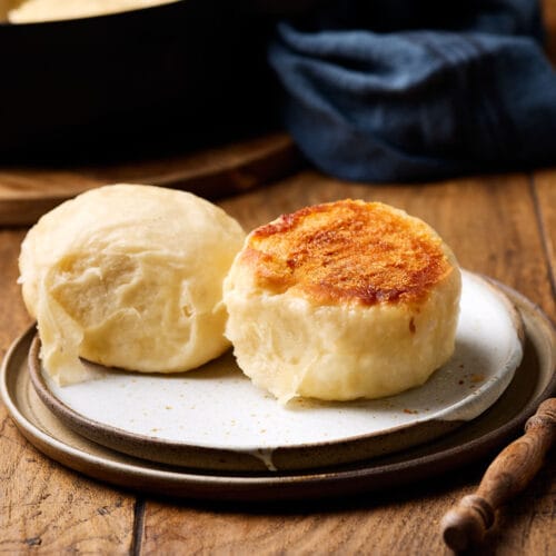 Dampfnudeln mit Salzkruste auf einem Teller mit einer Pfanne im Hintergrund.