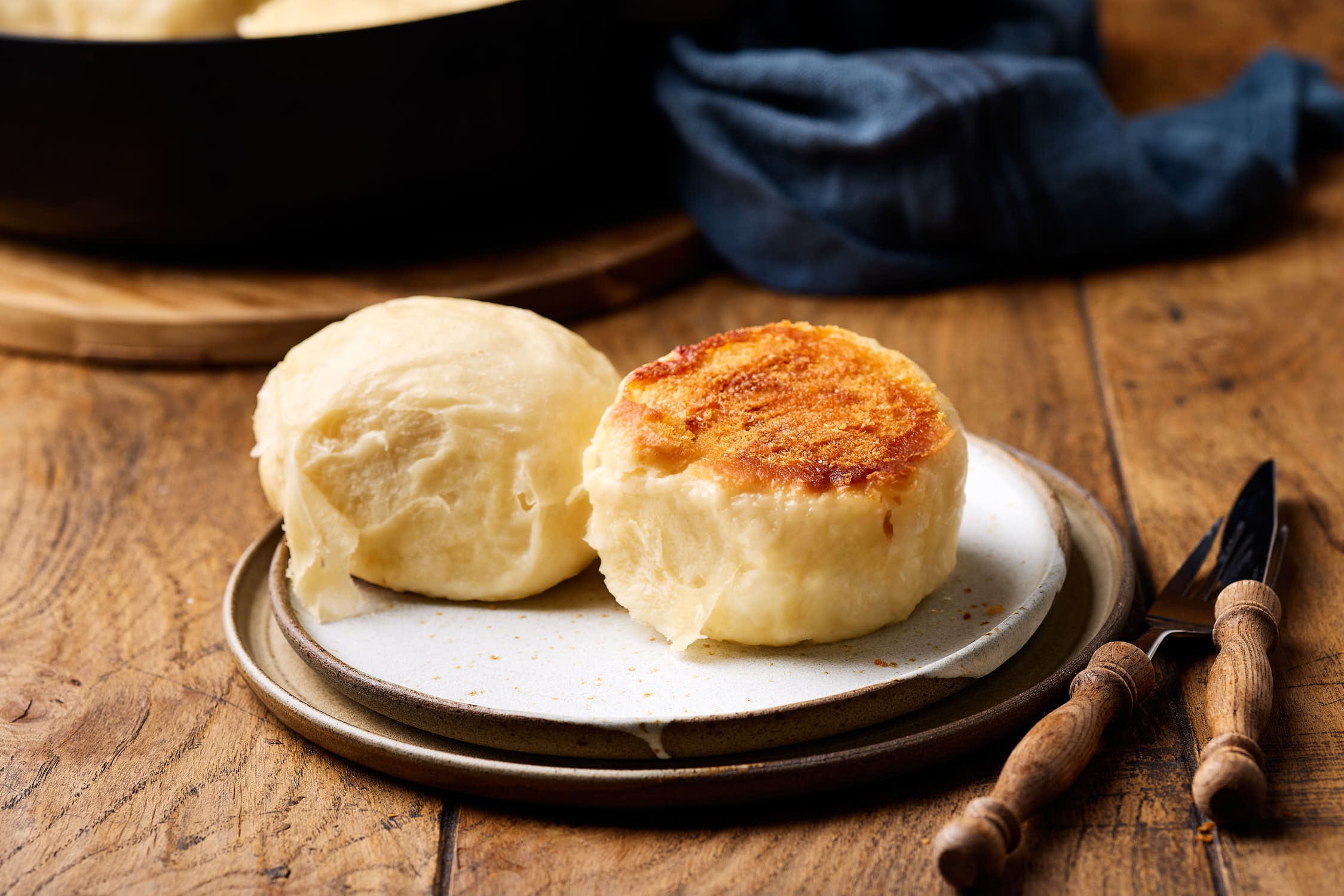 Dampfnudeln mit Salzkruste auf einem Teller mit einer Pfanne im Hintergrund.