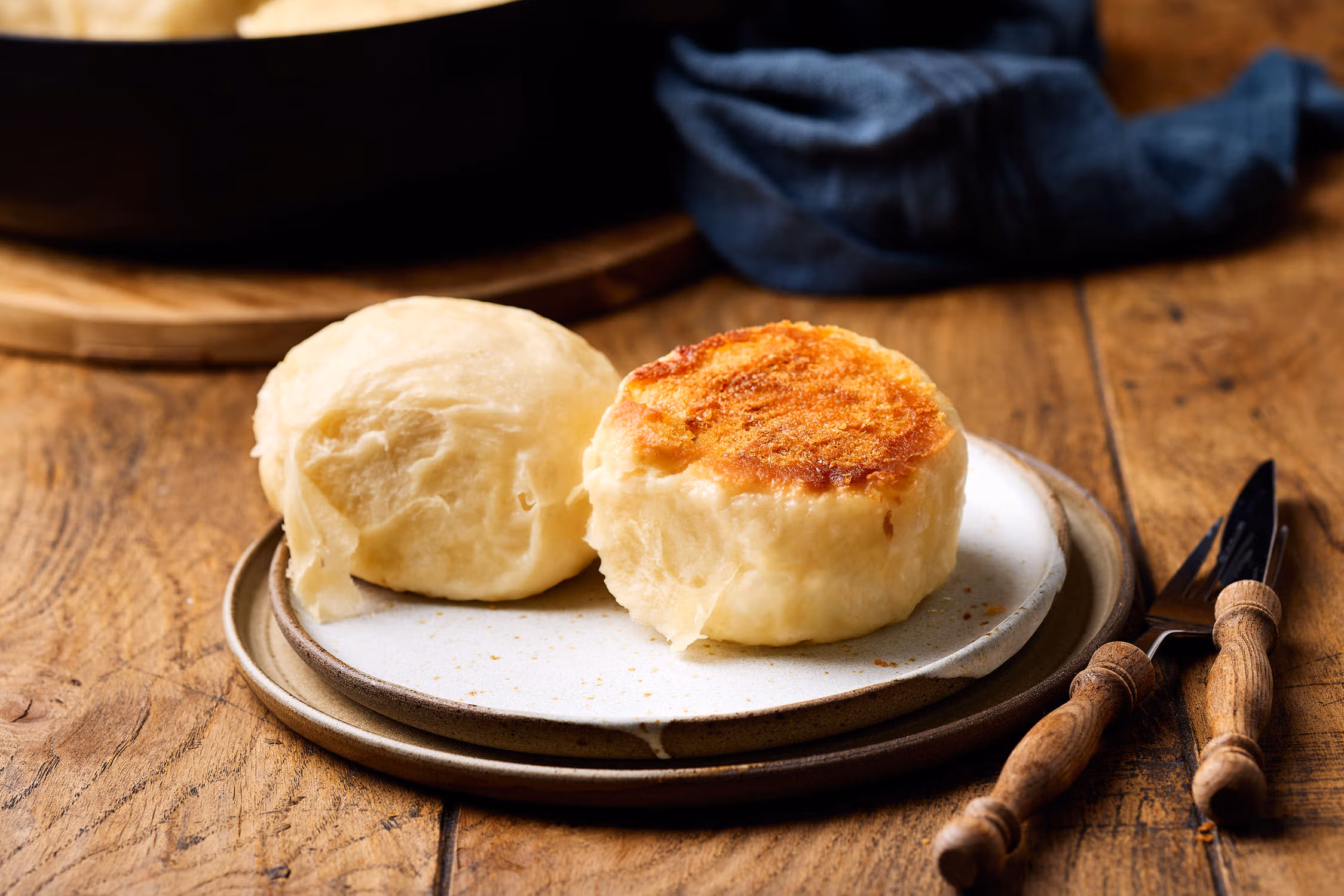 Dampfnudeln mit Salzkruste auf einem Teller mit einer Pfanne im Hintergrund.