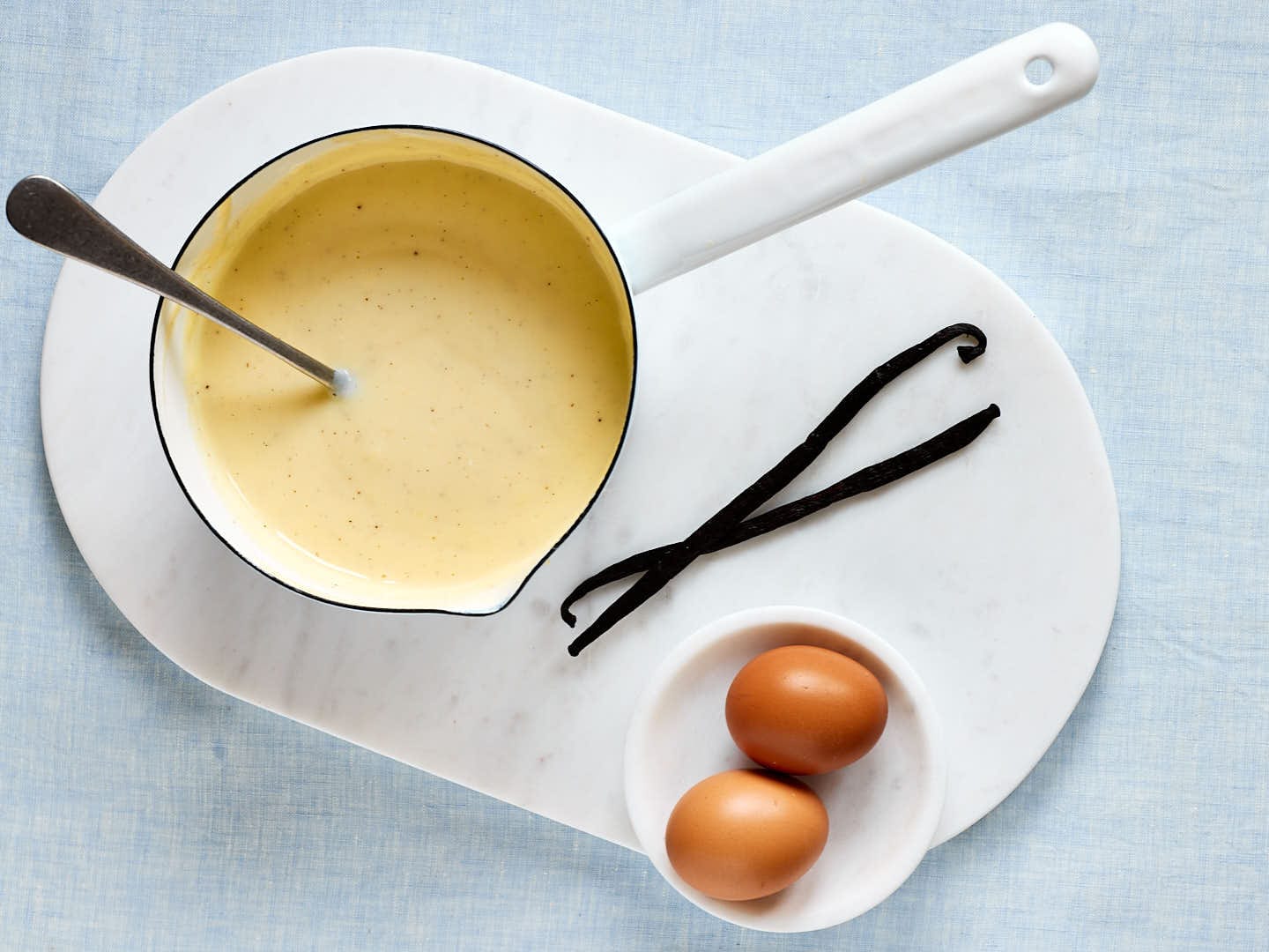 Selbstgemachte Vanillesoße wie von Oma – mit echter Vanille in einem Topf mit Vanilleschoten und Eiern daneben.