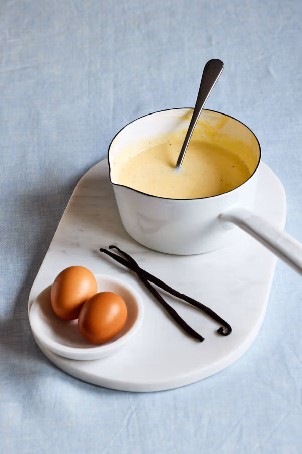 Selbstgemachte Vanillesoße wie von Oma – mit echter Vanille in einem Topf mit Vanilleschoten und Eiern daneben.
