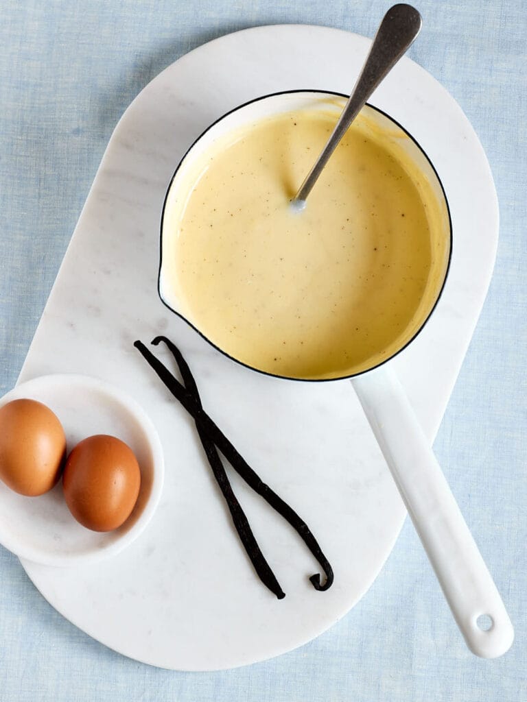 Selbstgemachte Vanillesoße wie von Oma – mit echter Vanille in einem Topf mit Vanilleschoten und Eiern daneben.