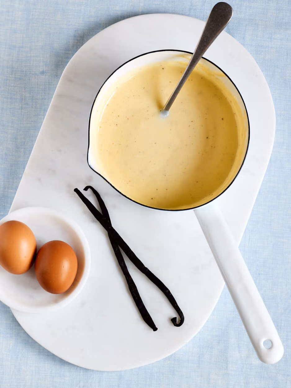 Selbstgemachte Vanillesoße wie von Oma – mit echter Vanille in einem Topf mit Vanilleschoten und Eiern daneben.