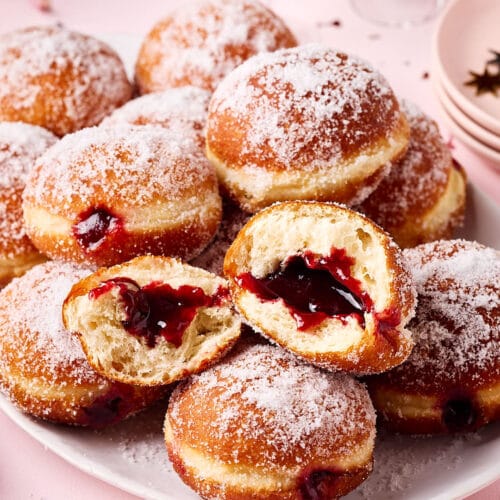 Frisch gebackene Berliner (Krapfen) aus Hefeteig, mit lockerer Krume und gefüllt mit Konfitüre, auf einer Servierplatte mit Silvesterdeko und Sektgläsern im Hintergrund.