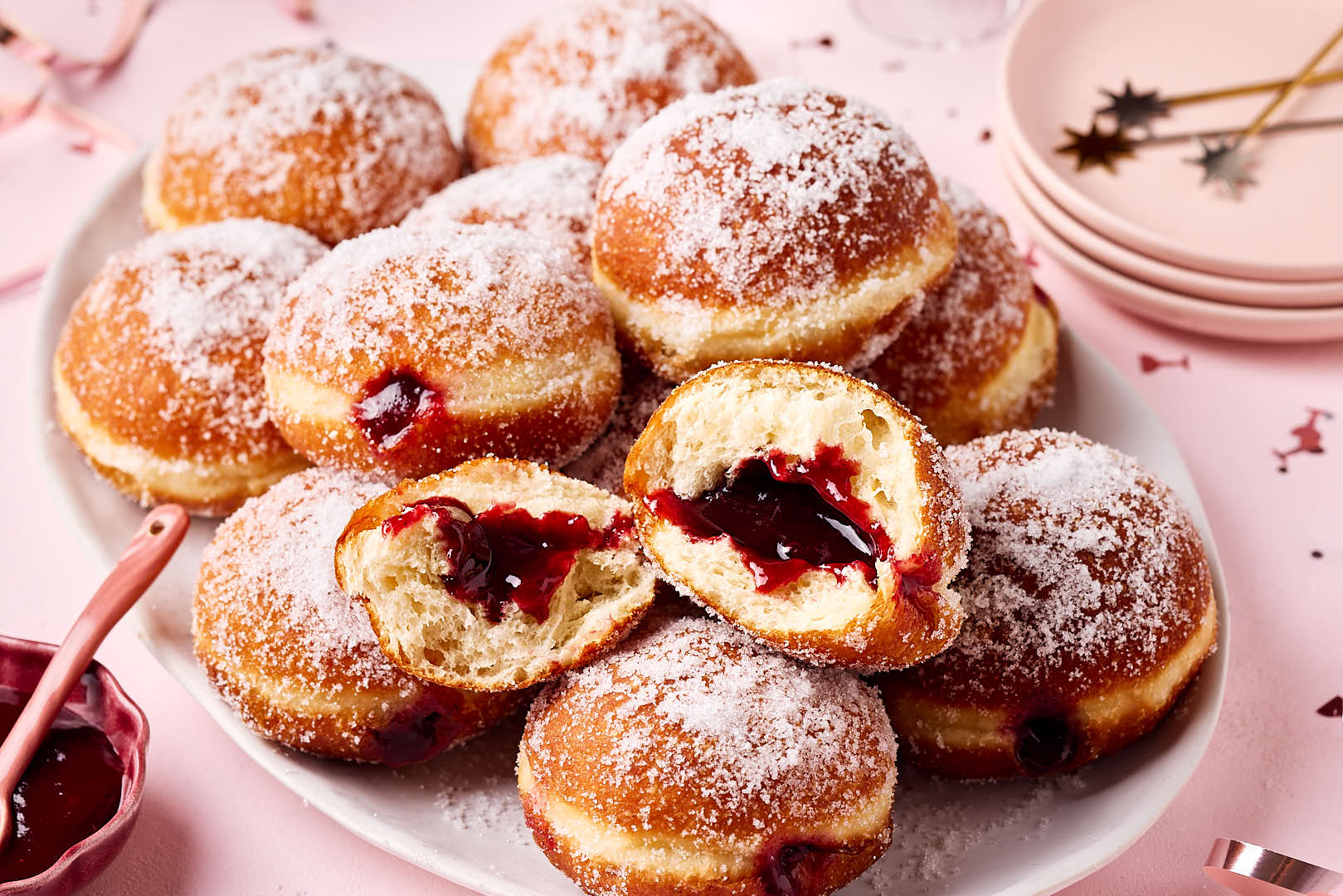 Frisch gebackene Berliner (Krapfen) aus Hefeteig, mit lockerer Krume und gefüllt mit Konfitüre, auf einer Servierplatte mit Silvesterdeko und Sektgläsern im Hintergrund.