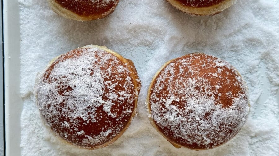 Frisch frittierte Berliner in Zucker wälzen.