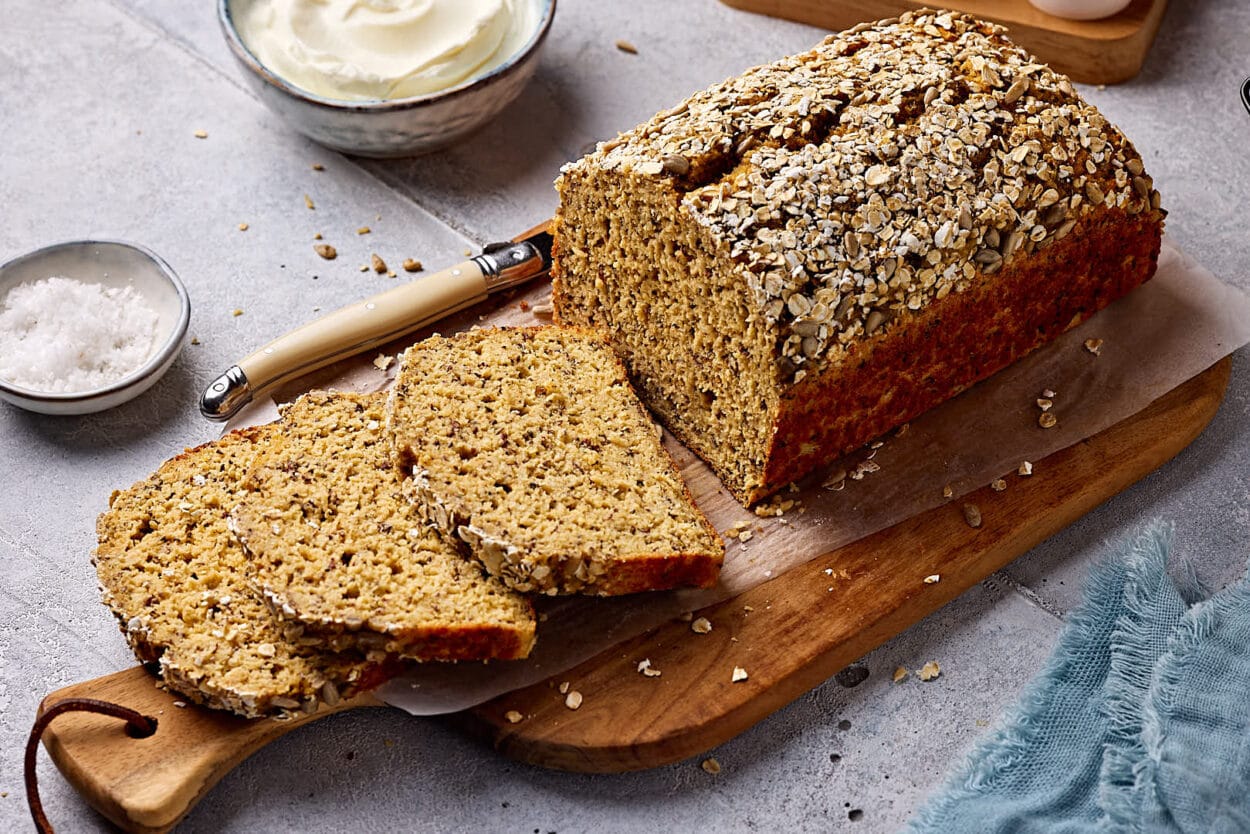 Schnelles Eiweißbrot mit Quark, aufgeschnitten auf einem Holzbrett mit Quark und Salz im Hintergrund.