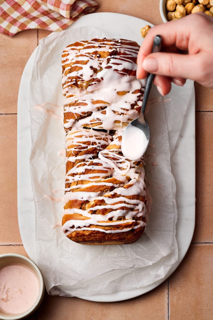 Saftiger Nusszopf auf einem Marmortablett mit Puderzucker-Guss, der gerade aufgetragen wird. .