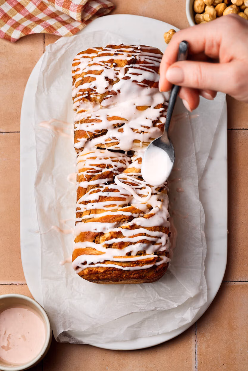 Saftiger Nusszopf auf einem Marmortablett mit Puderzucker-Guss, der gerade aufgetragen wird. .
