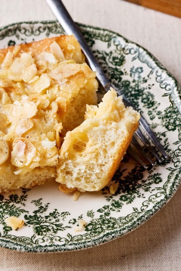 Nahaufnahme von Omas Butterluchen mit Sahneguss und Mandel-Zucker-Topping auf einem Teller mit lockerer Krume.