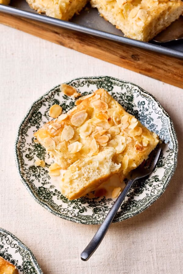 Nahaufnahme von Omas Butterluchen mit Sahneguss und Mandel-Zucker-Topping auf einem Teller mit lockerer Krume.