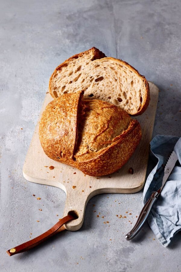 Brot backen mit Sauerteig: rustikales Sauerteigbrot mit lockerer Krume, aufgeschnitten auf einem Holzbrett.
