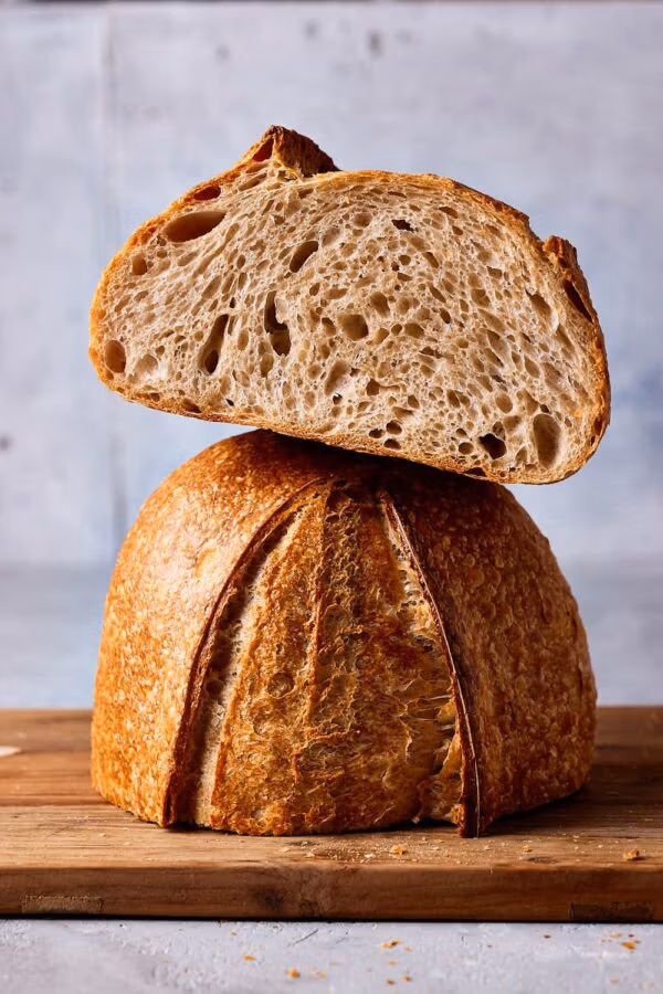 Anschnitt eines lockeren Weizensauerteigbrotes auf einem Holzbrett, das die grobe Porung der Krume und die knusprige Kruste zeigt, gebacken ohne Knetmaschine nach einem einfachen Anfänger-Rezept.